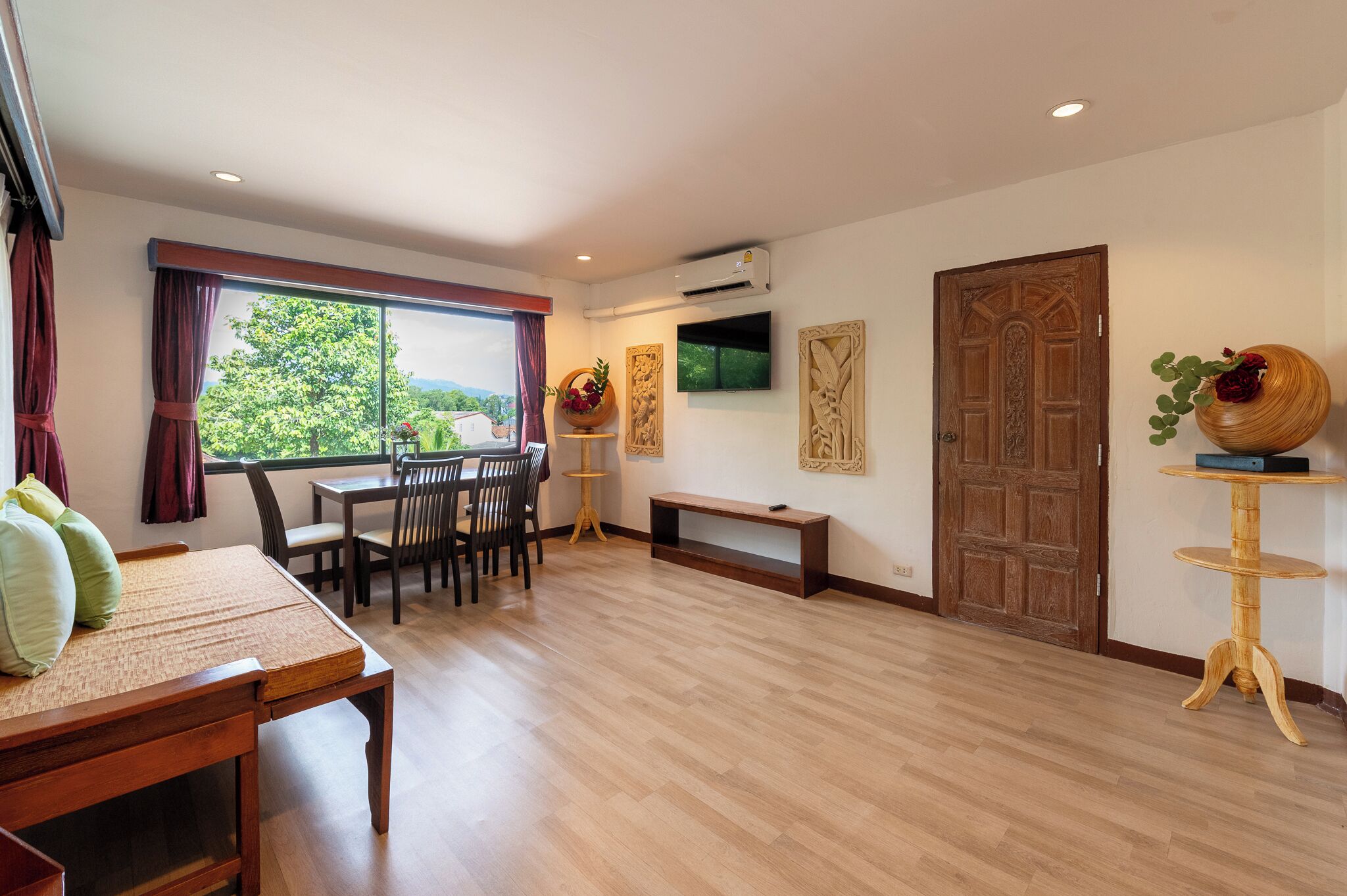 A spacious room with a wooden dining table, chairs, and a large window offering a view of greenery.