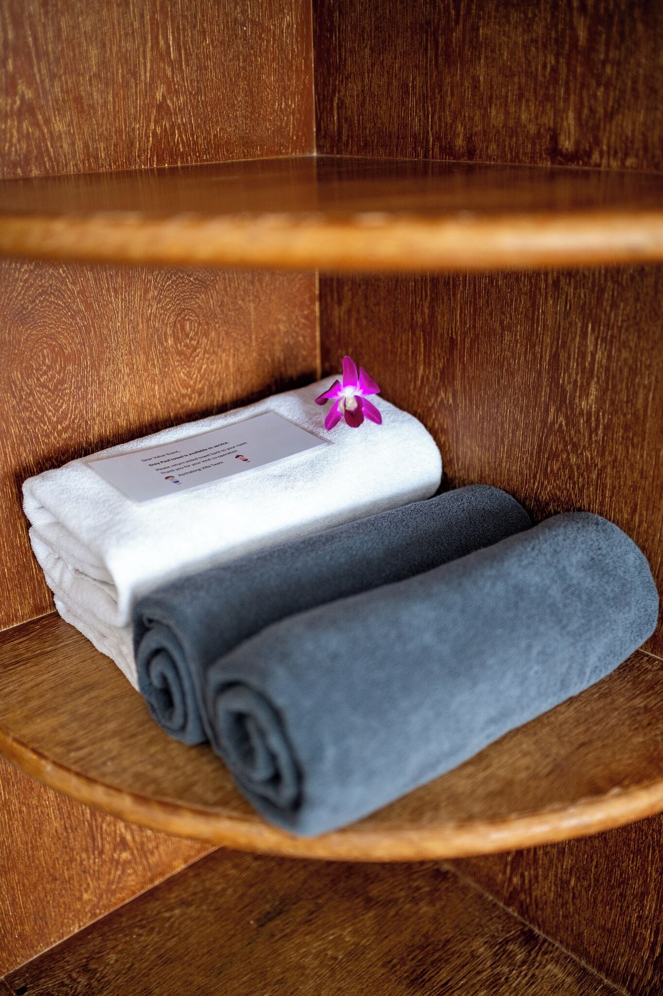 A wooden shelf with folded towels and a card.