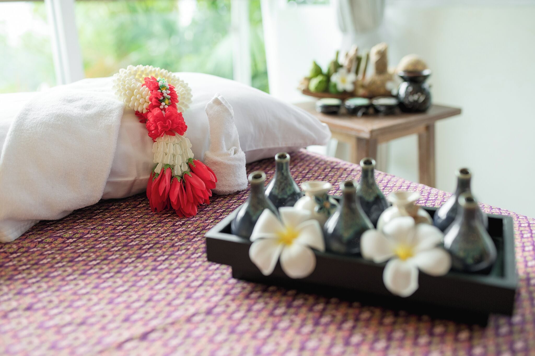 A neatly made bed with a white pillow and a decorative floral arrangement. A tray with small vases and a white flower is placed on the bed.