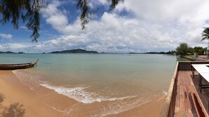 A beach with a wooden boat, a wooden deck, and a view of the sea and distant islands. - Aochalong Villa Resort & Spa (Chalong)