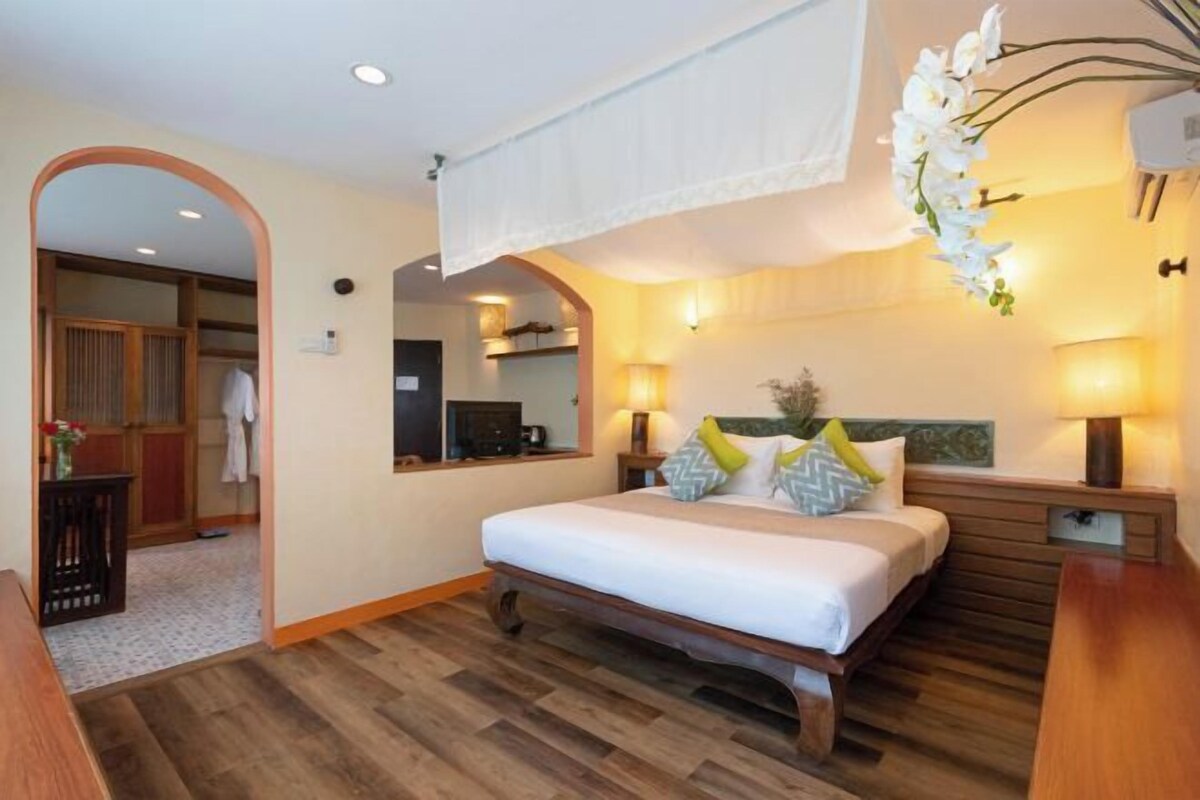 A hotel room with a large bed, wooden floor, a mirror, and a wardrobe.