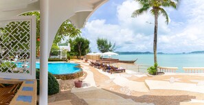 A pool area with lounge chairs, a palm tree, and a view of the sea. - Aochalong Villa Resort & Spa (Chalong)