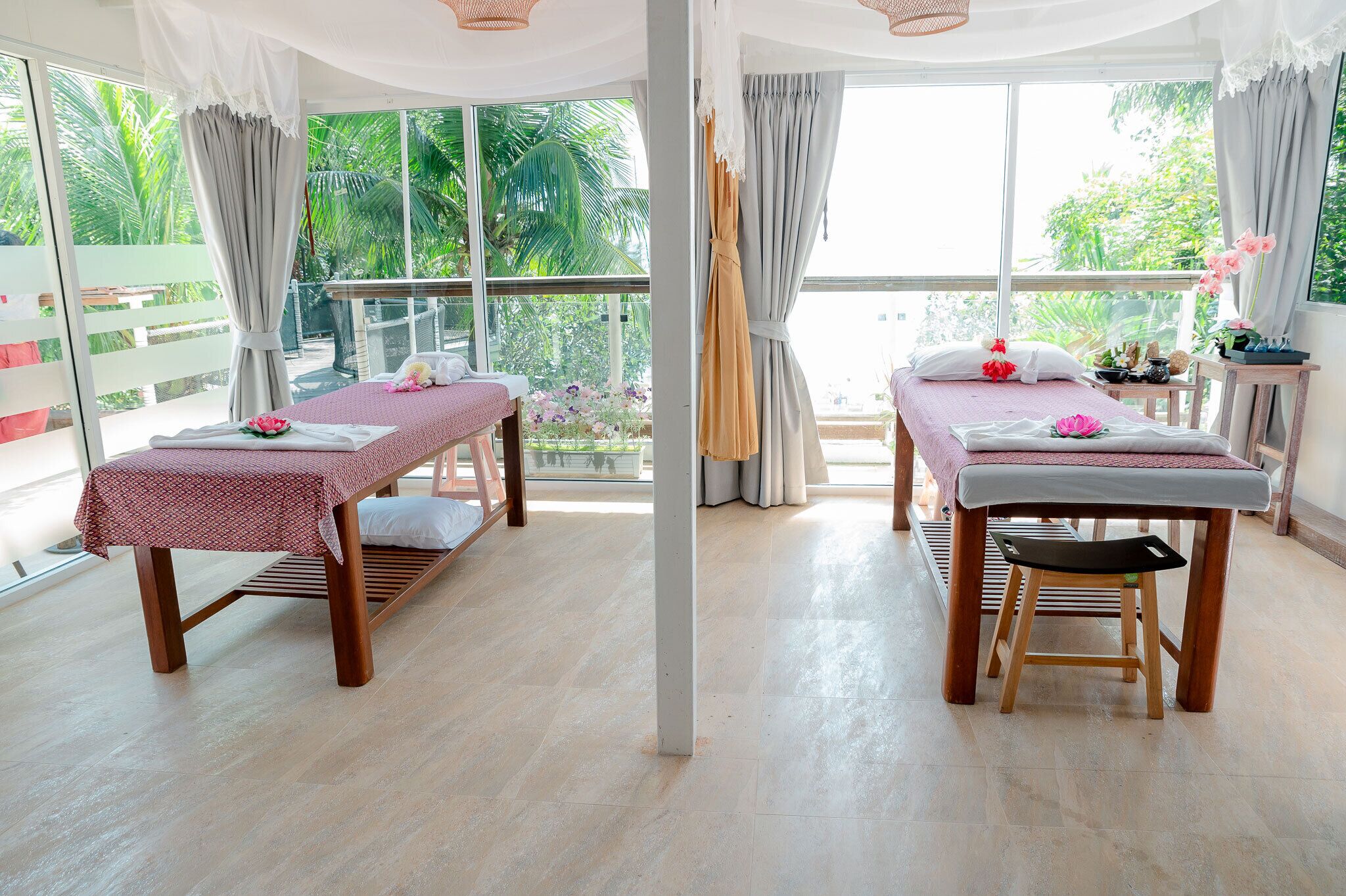 Une pièce dotée de deux tables de massage, de grandes fenêtres et offrant une vue sur la verdure environnante.