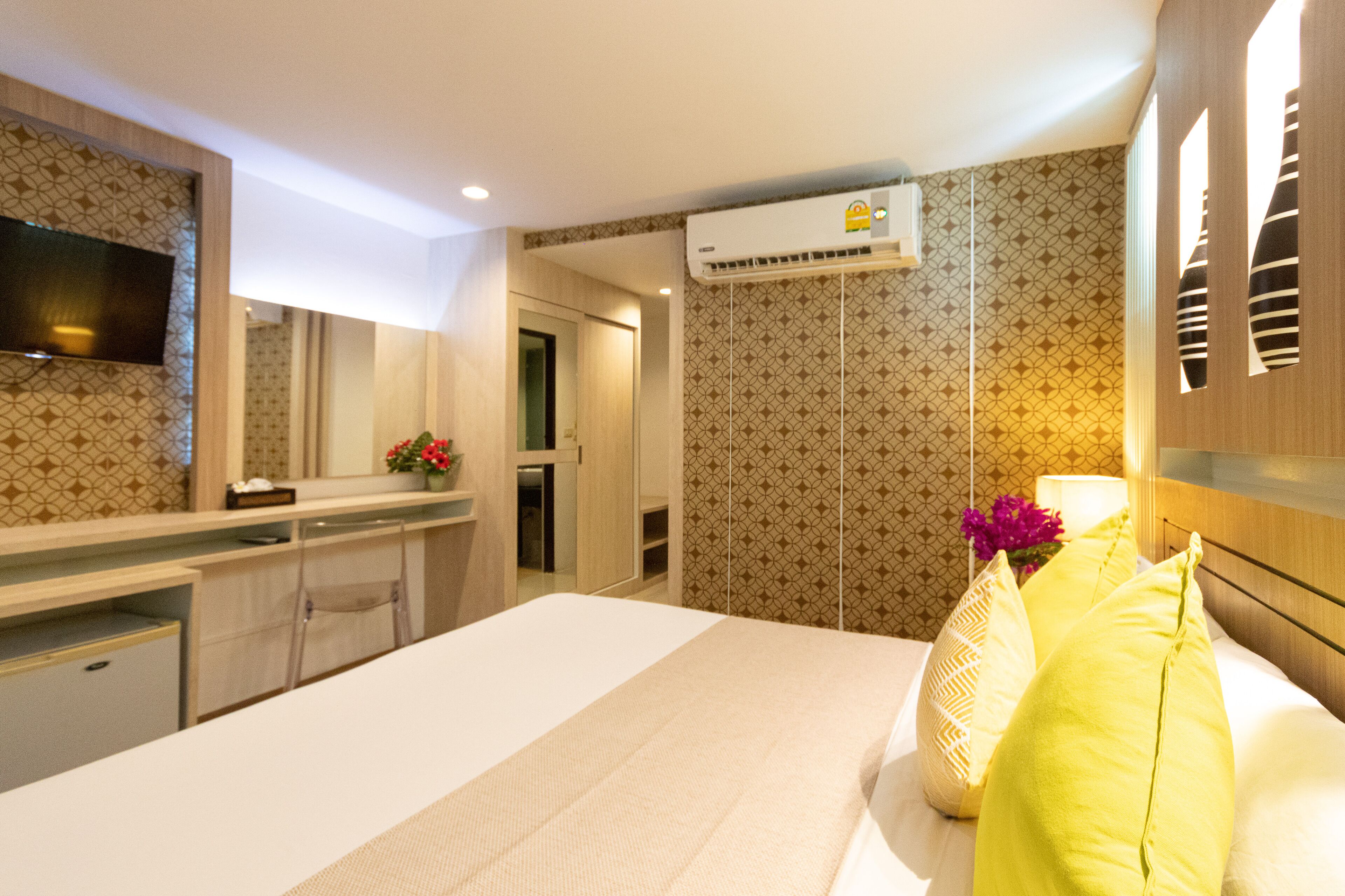 A hotel room with a bed, a desk, a mirror, an air conditioning unit, and patterned wallpaper.