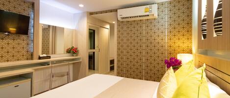 A hotel room with a bed, a desk, a mirror, an air conditioning unit, and patterned wallpaper.