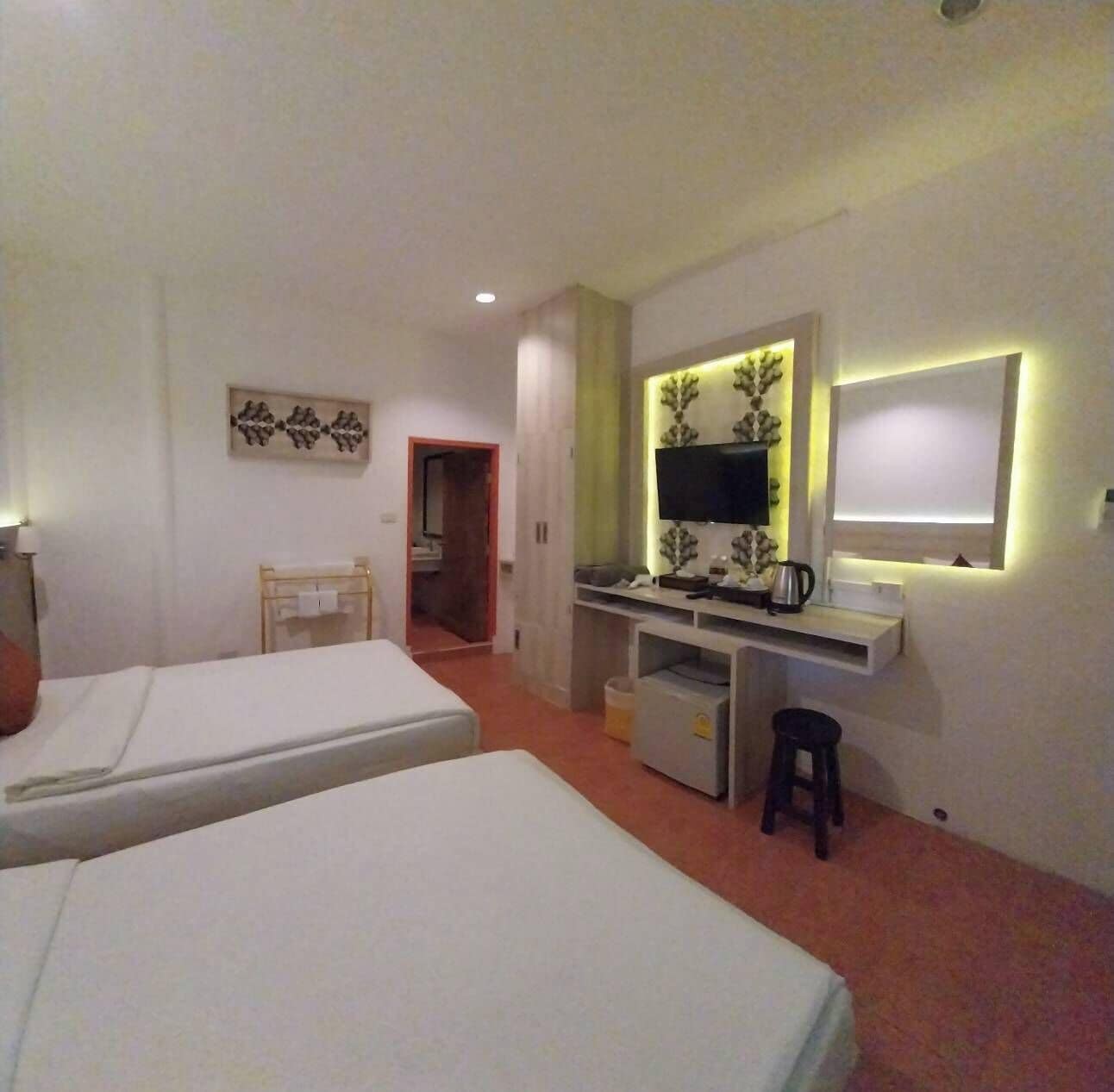 Ein Hotelzimmer mit zwei Betten, einem Schreibtisch mit Fernseher, einem kleinen Hocker und einem Spiegel.