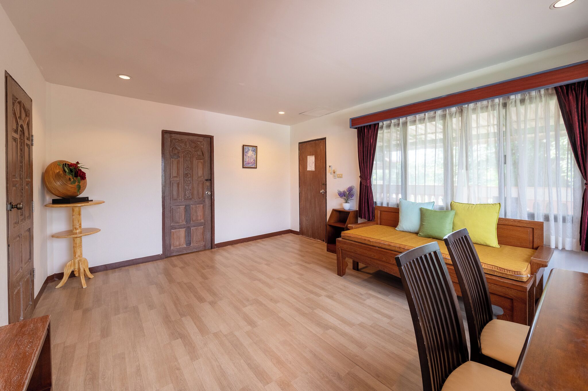 A spacious room with a wooden floor, a wooden sofa with cushions, a small round table, and a wooden cabinet.
