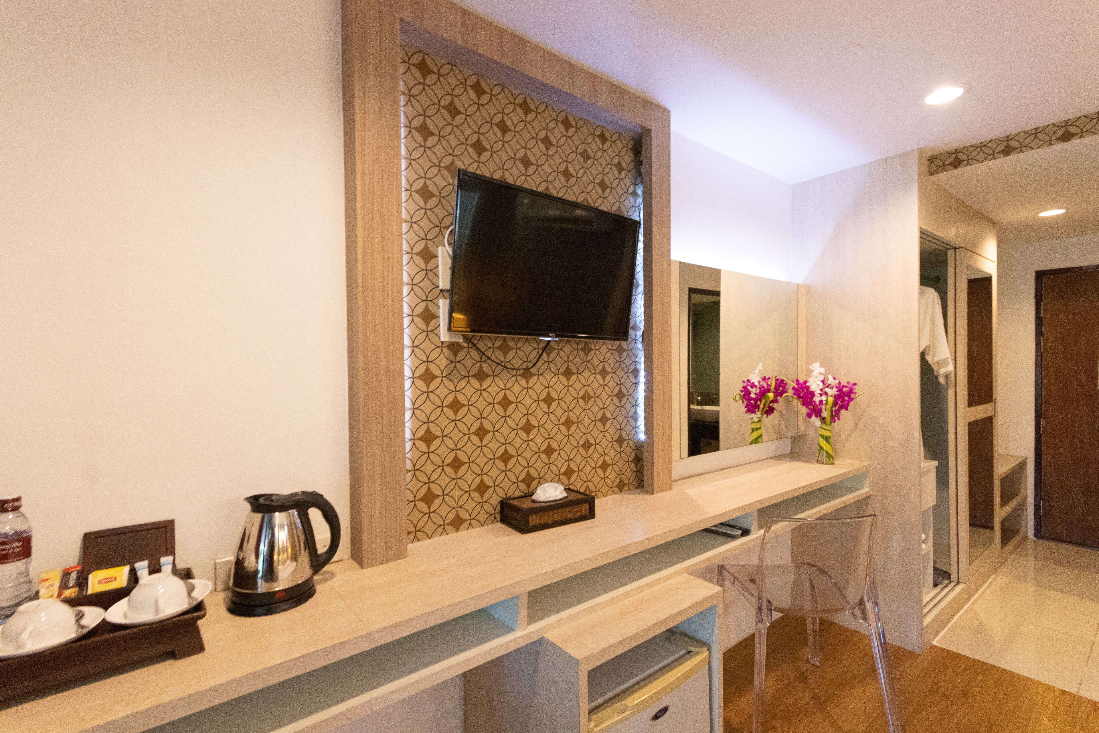 A modern bathroom with a large mirror, a mounted TV, and a vanity area with a coffee maker and toiletries.