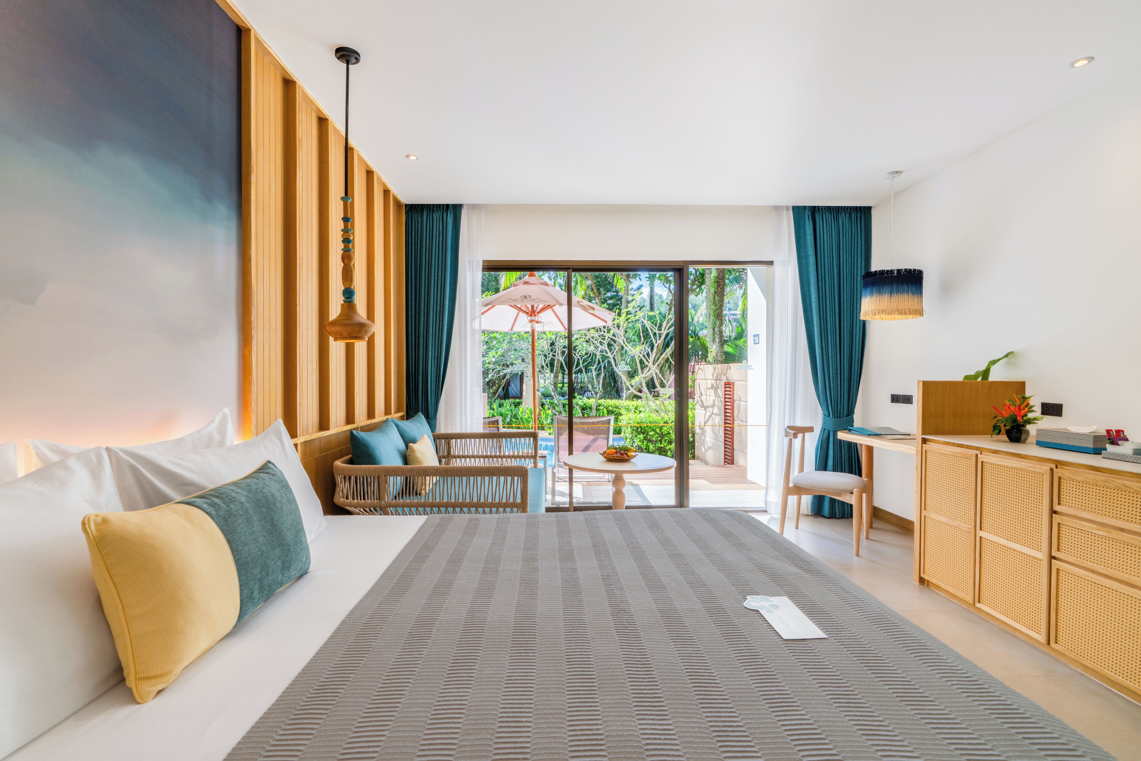 A modern hotel room with a bed, seating area, dining table, and a view of the outdoors.