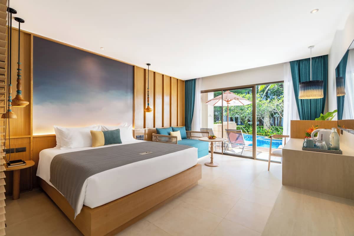 A modern hotel room with a large bed, a seating area with a view of the pool, and a reception desk.
