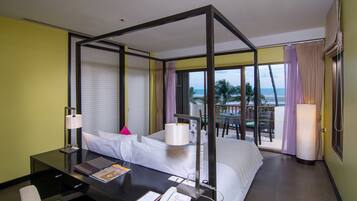 Habitación de hotel con balcón, cama, escritorio con lámpara y vista a la playa.