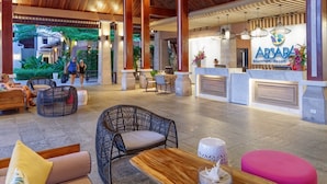 Un lobby espacioso con techo alto, vigas de madera y lámparas colgantes de colores. Hay una recepción con un cartel que dice "ABSARA Beachfront Resort".