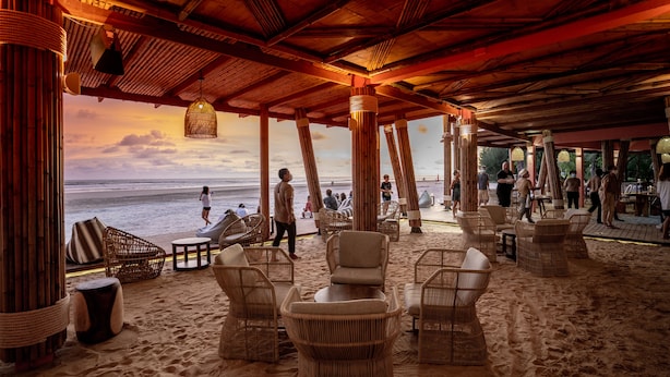 Un salón frente a la playa con muebles de mimbre, techo de madera y vista al océano.
