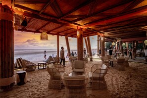 Un salon de plage doté de meubles en osier, d’un plafond en bois et offrant une vue sur l’océan.