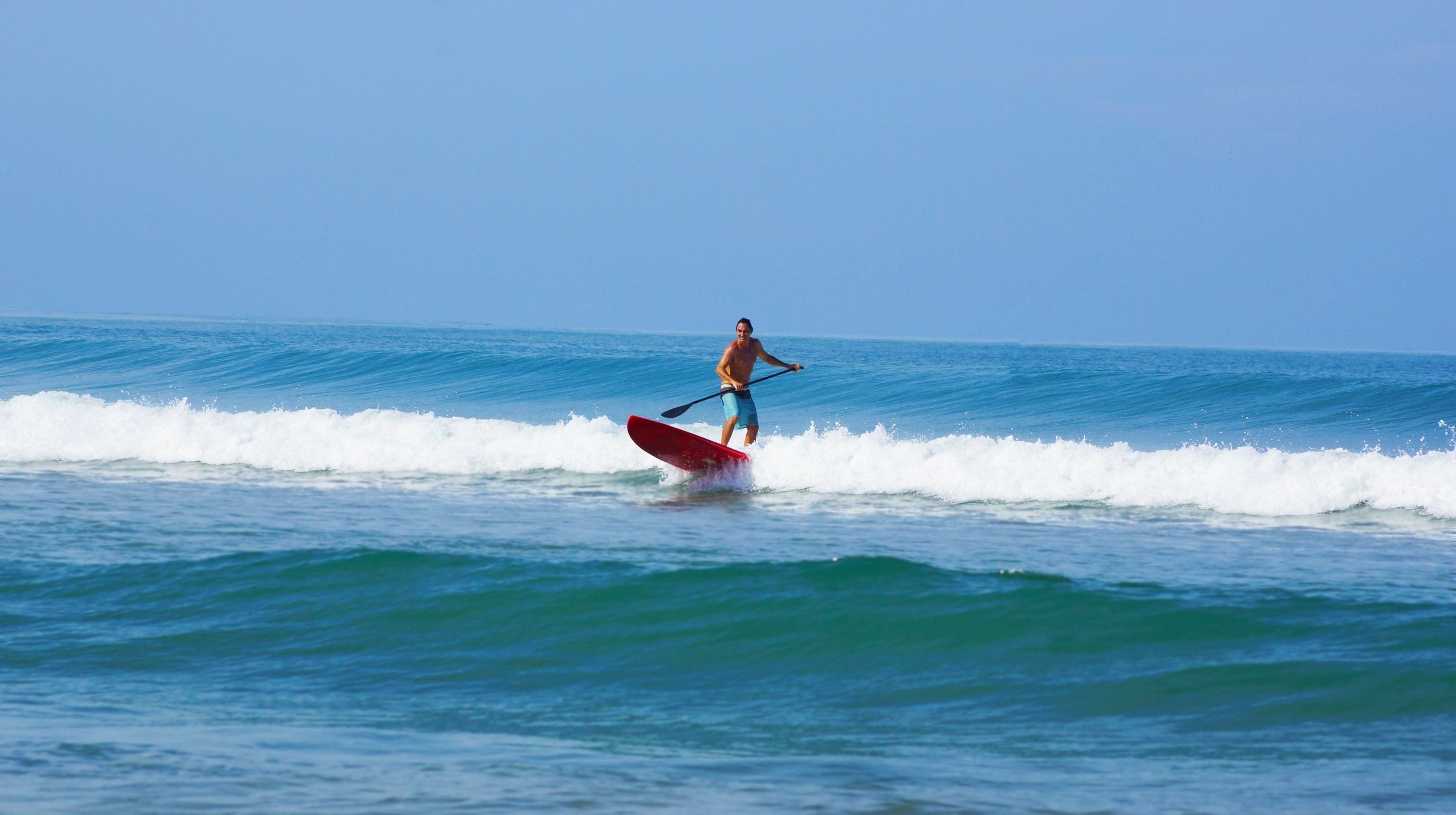 Una persona haciendo paddleboard sobre un mar tranquilo con olas.