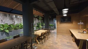 A restaurant with a long counter, wooden chairs, and a stone wall with plants. - The Bedrooms Boutique Hotel (Bangkok)