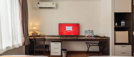 A hotel room with two beds, a desk, a chair, a TV, an air conditioner, a trash bin, and a minibar.