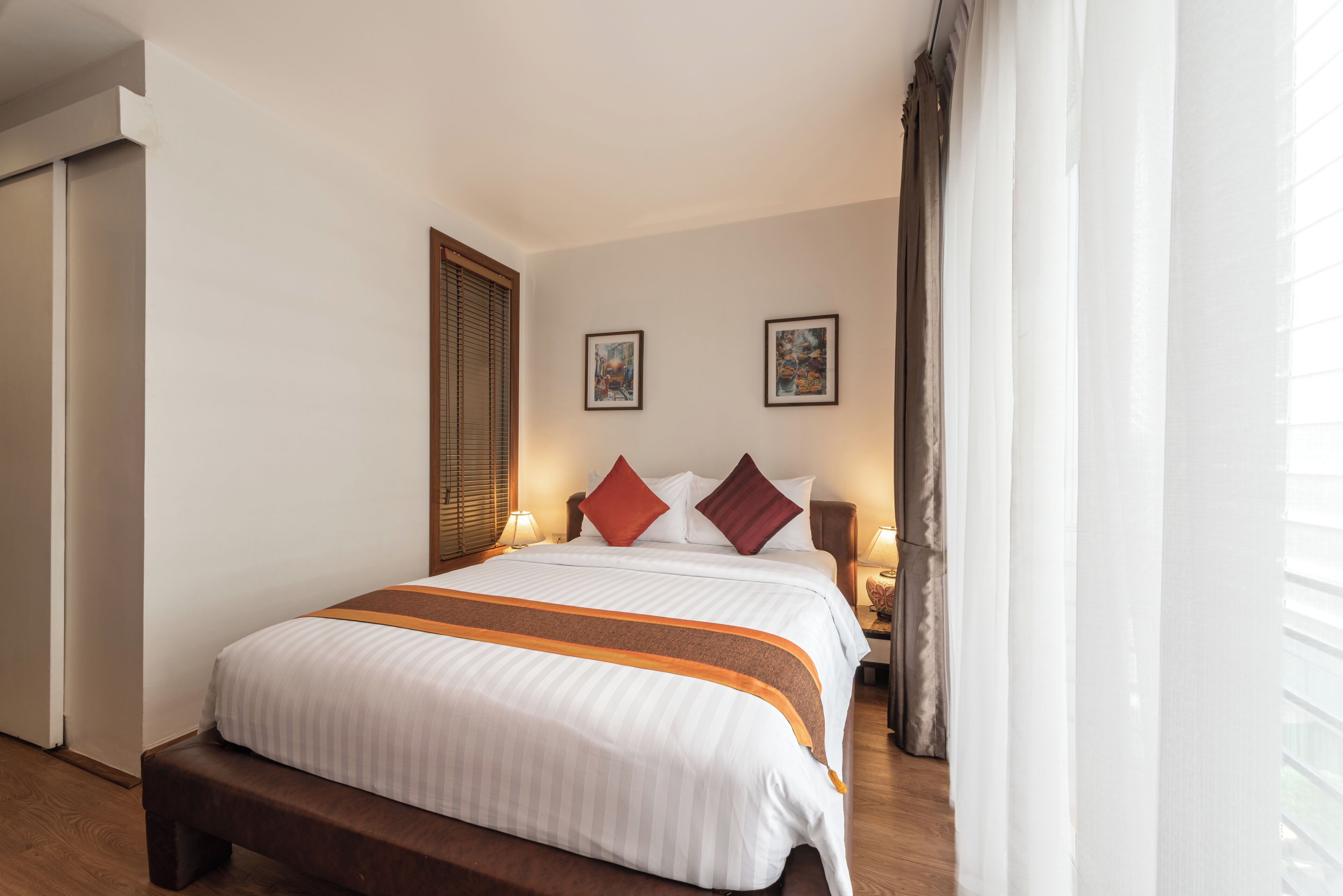 A hotel room with a large bed, wooden bench, two bedside tables with lamps, and two framed pictures on the wall.
