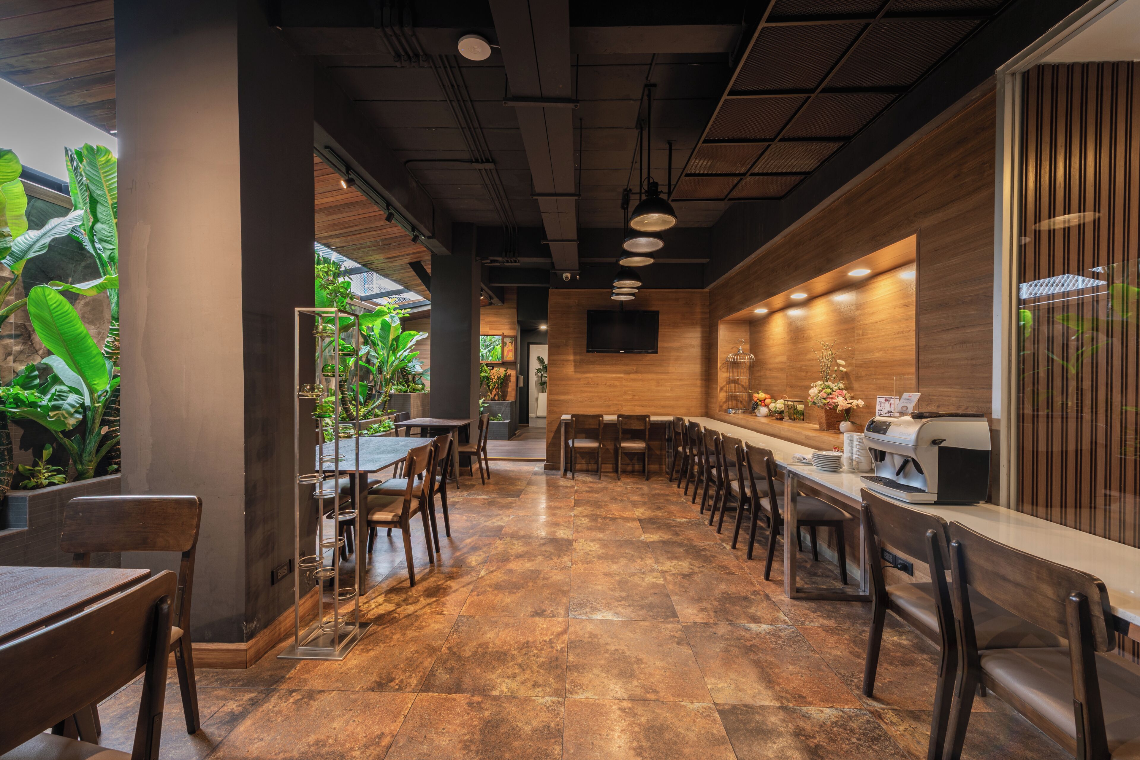 A restaurant with a long counter, multiple seating areas, and a view of indoor plants.