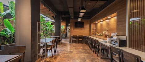 A restaurant with a long counter, multiple seating areas, and a view of indoor plants.