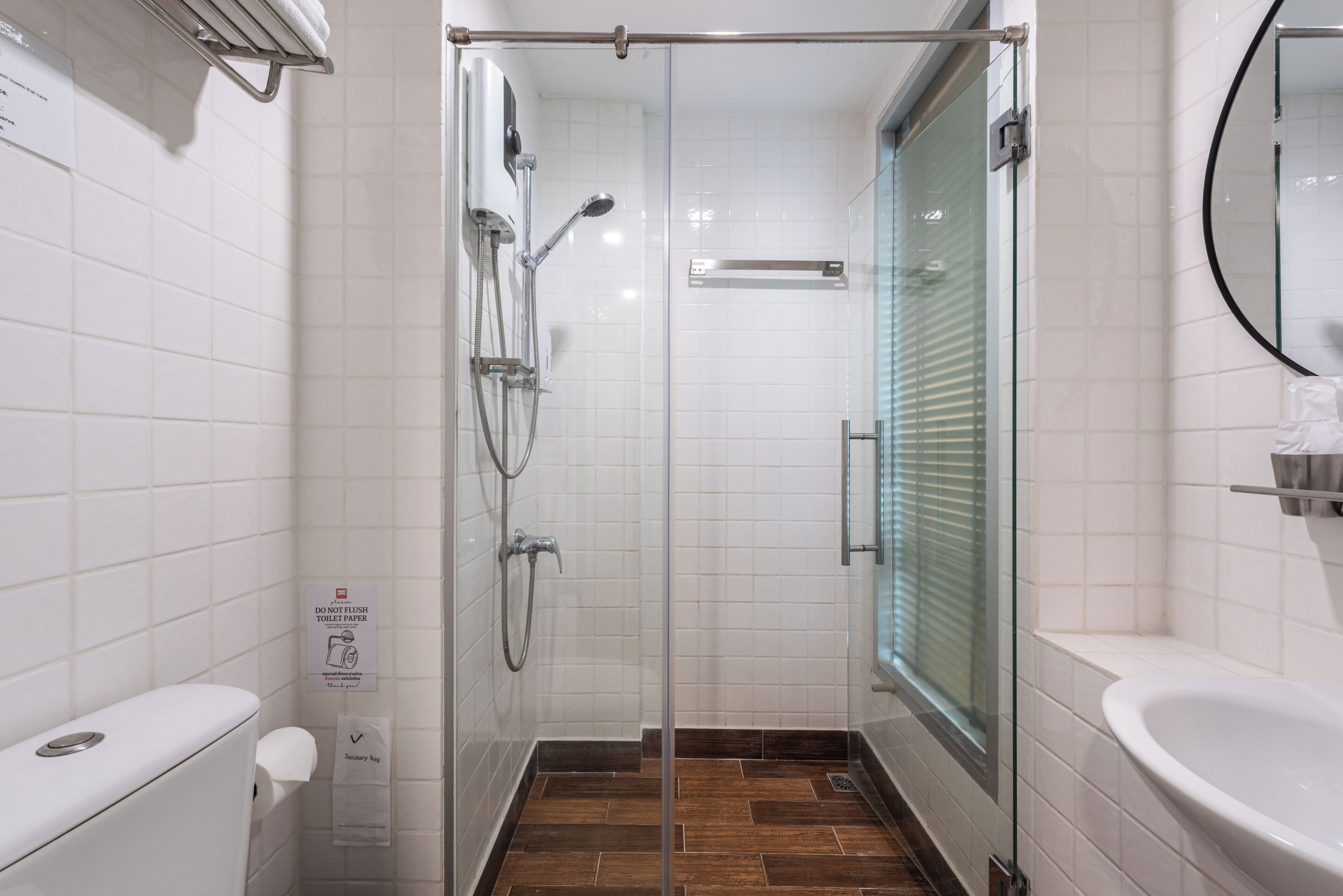 A glass-enclosed shower stall with a white tiled wall, a glass door, and a white sink with a mirror.
