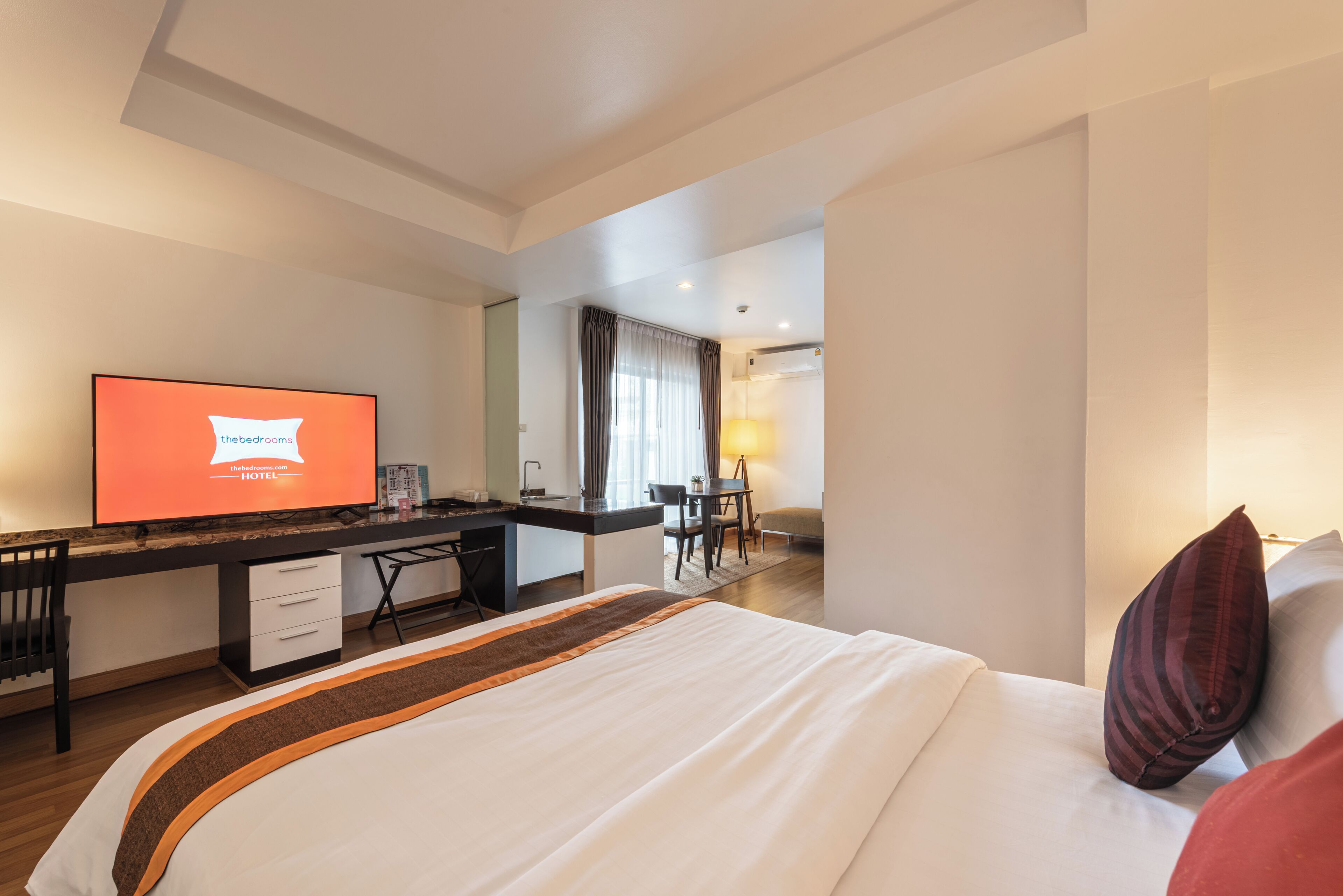 A hotel room with a bed, a desk, a television, and a view of the hallway.