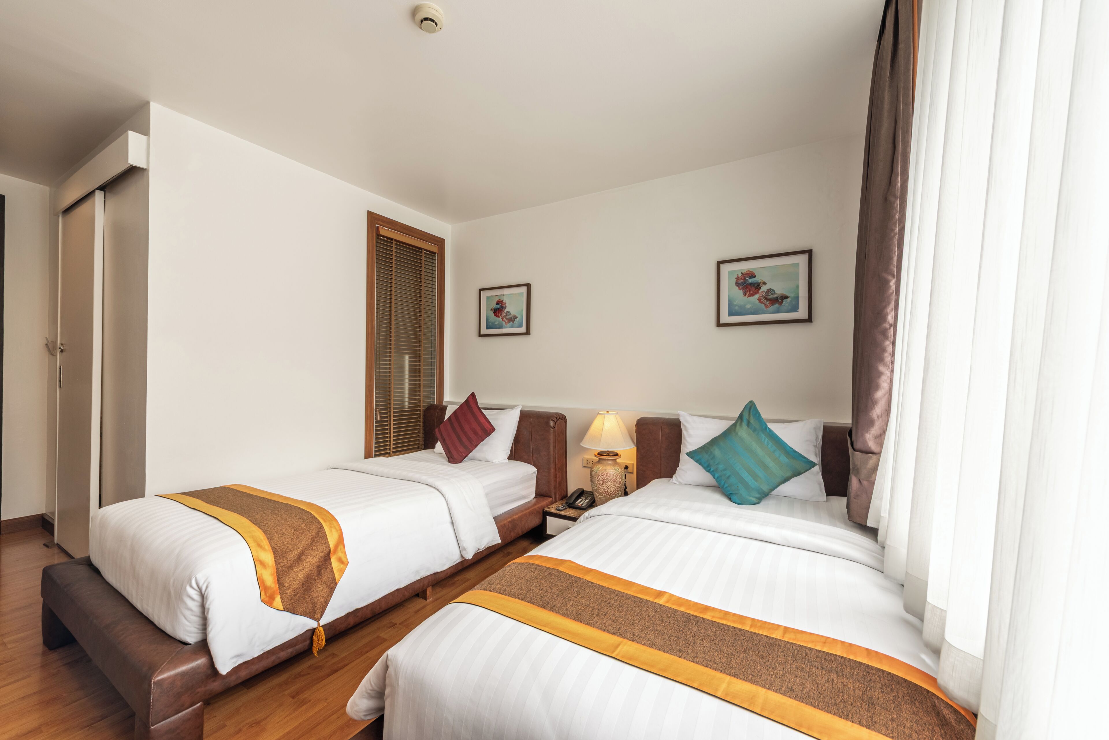 Een hotelkamer met twee bedden, een nachtkastje met lamp, een raam met gordijnen en een deur.