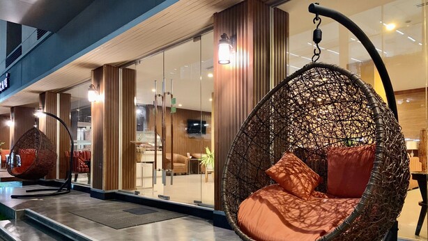 A modern interior with a glass wall, a hanging chair with a cushion, and a staircase leading to an upper level. - The Bedrooms Boutique Hotel (Bangkok)