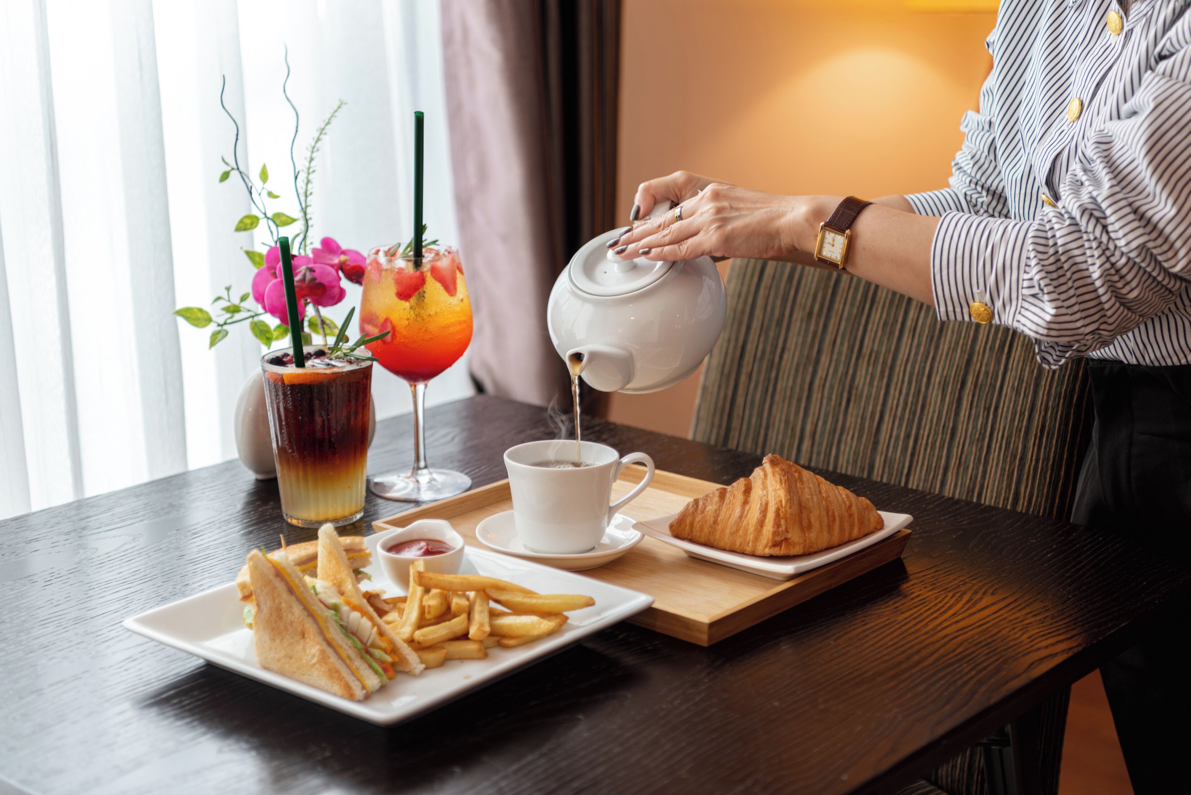 A table with a croissant, a sandwich, fries, and a drink.