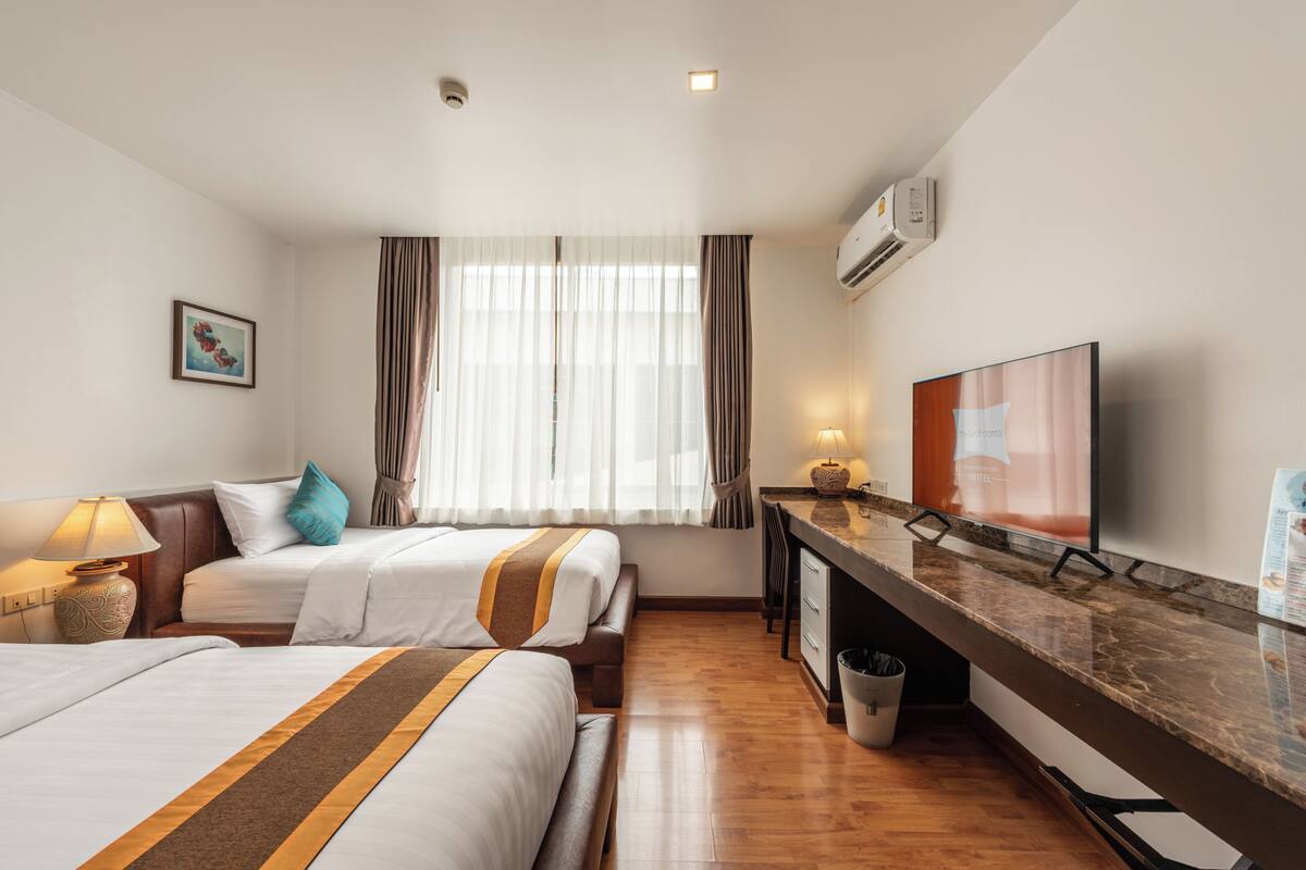 A hotel room with two beds, a desk, a television, and a window with curtains.