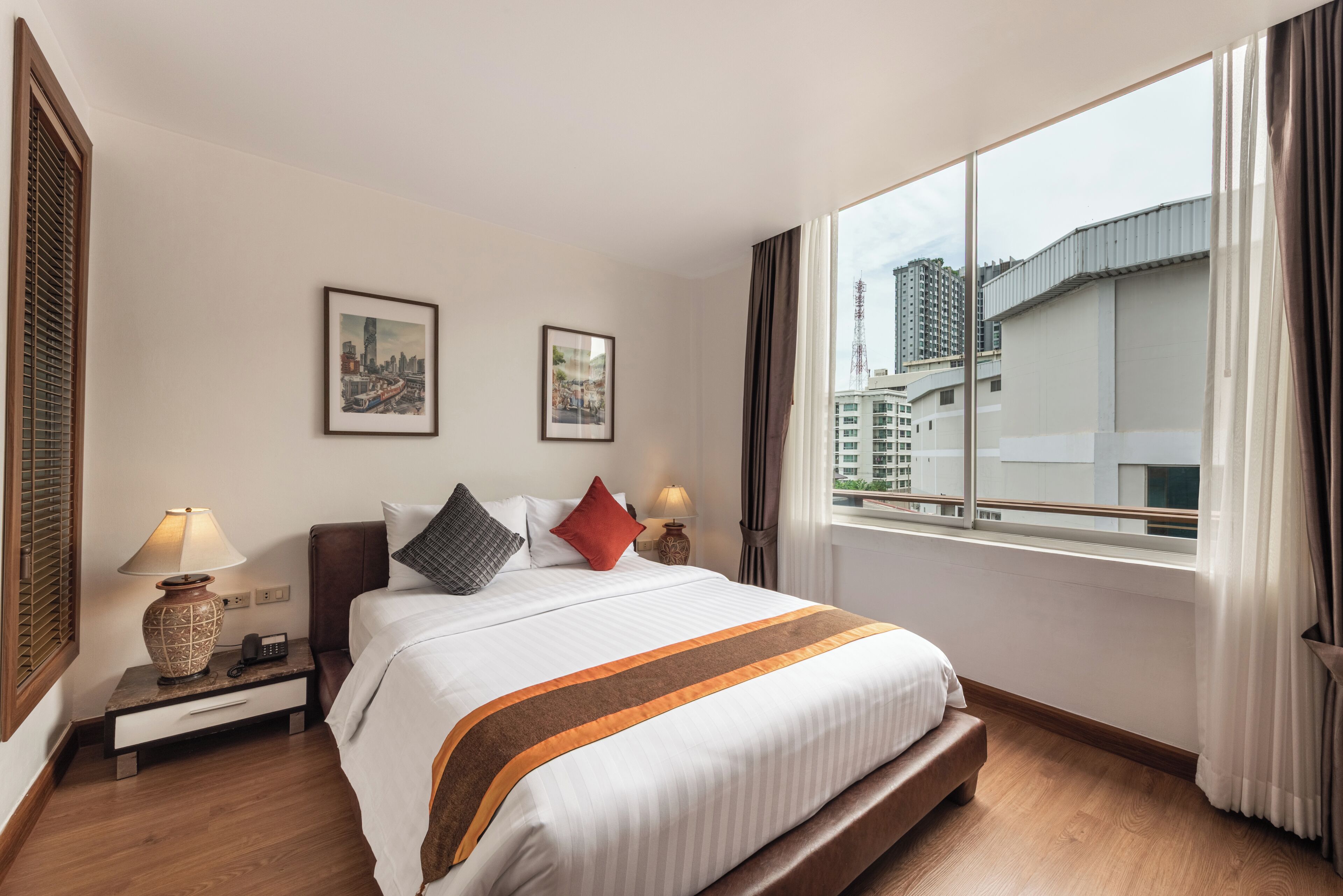 Habitación de hotel con cama, mesitas de noche, ventana con cortinas y dos cuadros en la pared.