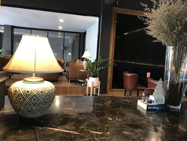 Un hall moderno con piso de mármol, una lámpara decorativa grande, una planta en maceta, una estantería con libros y un espejo amplio.