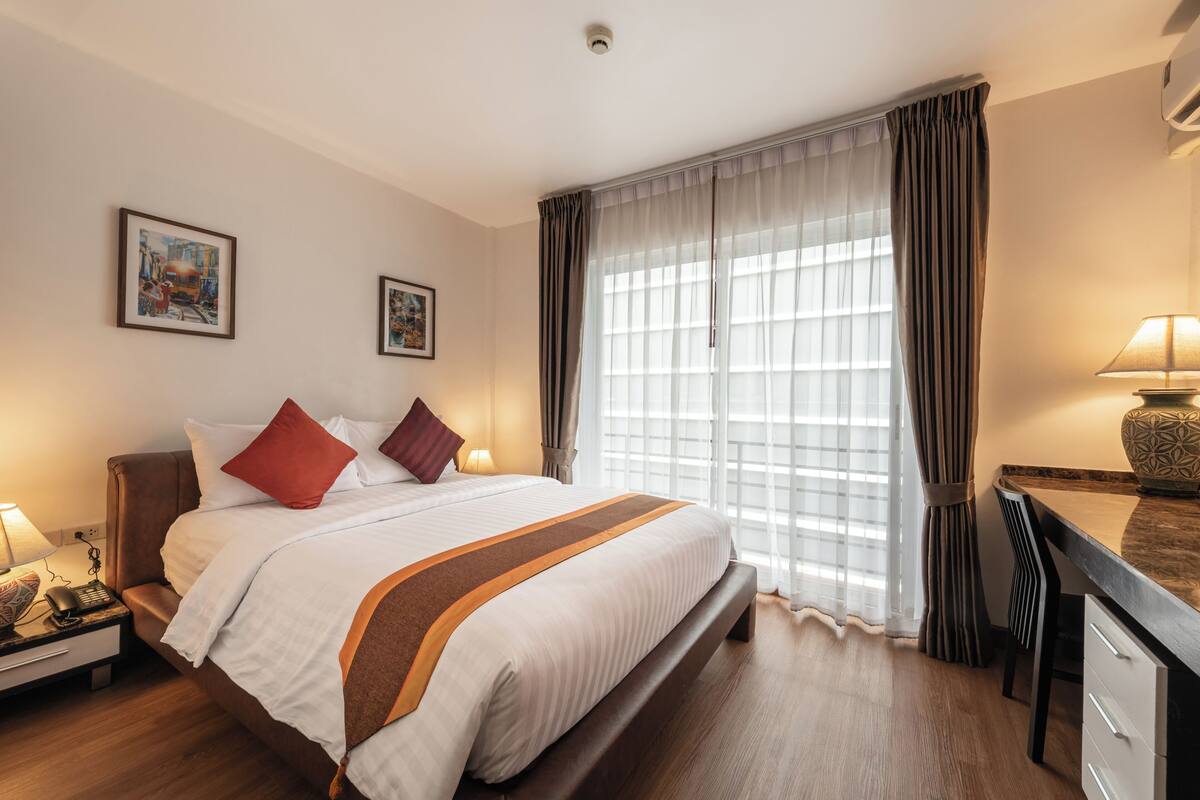 A hotel room with a bed, bedside table, lamp, and a large window with curtains.