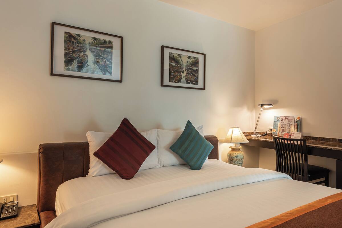 A hotel room with a bed, two framed pictures on the wall, a desk with a lamp, and a chair.