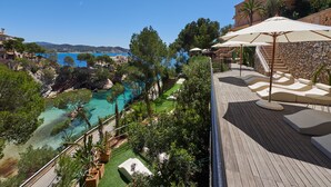 A wooden deck with lounge chairs and umbrellas overlooking a clear blue pool and a scenic view of the coastline. - Hotel Petit Cala Fornells (Calvia)