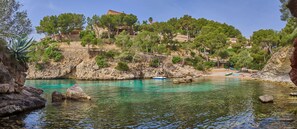 A coastal area with clear turquoise water, rocky terrain, and buildings on a hillside. - Hotel Petit Cala Fornells (Calvia)