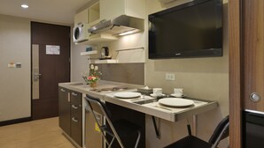 A compact kitchen with a microwave, stove, and a flat-screen TV mounted above the counter. - Arawana Express Phromphong (Bangkok)