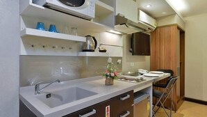 A modern kitchen with a built-in microwave, a sink, and a stove. There are cabinets above the counter and a wooden cabinet to the right. - Arawana Express Phromphong (Bangkok)