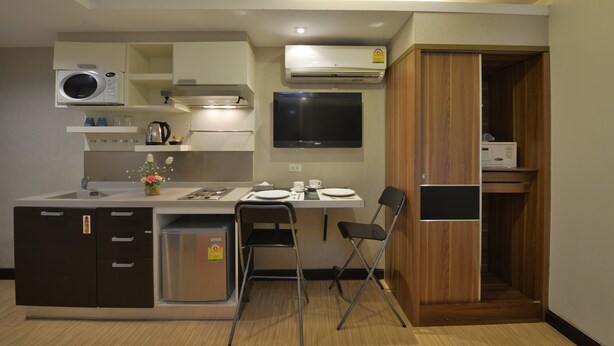 A compact kitchen with a microwave, stove, sink, and a small refrigerator. There is a dining area with a table and chairs, and a TV mounted on the wall. - Arawana Express Phromphong (Bangkok)