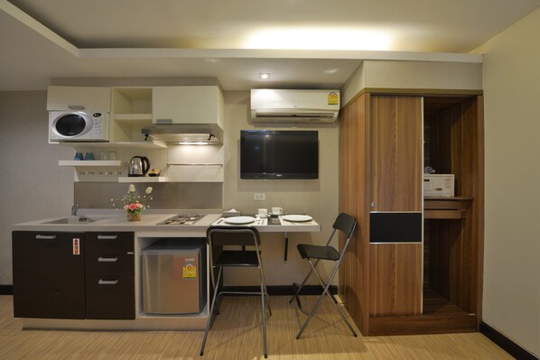 Une cuisine compacte équipée d’un four à micro-ondes, d’une cuisinière, d’un évier et d’un petit réfrigérateur. On y trouve également un coin repas avec une table et des chaises, ainsi qu’un téléviseur fixé au mur.