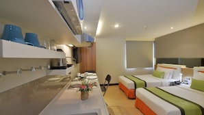 A hotel room with a kitchenette, two beds with green and white bedding, a small dining table, and a window. - Arawana Express Phromphong (Bangkok)