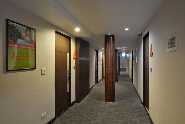 A hotel corridor with doors, a large pillar, and a poster on the wall. - Arawana Express Phromphong (Bangkok)