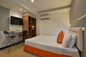 A hotel room with a bed, a desk, a chair, a wardrobe, and an air conditioning unit. - Arawana Express Phromphong (Bangkok)