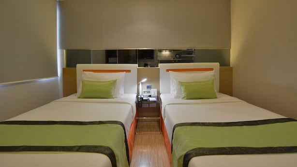 A hotel room with two single beds, a small table with a lamp, and a mirror above the bed. - Arawana Express Phromphong (Bangkok)