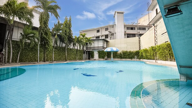 A swimming pool with clear blue water, surrounded by palm trees and a building with a white facade. - Pattaya Hiso Hotel (Pattaya)