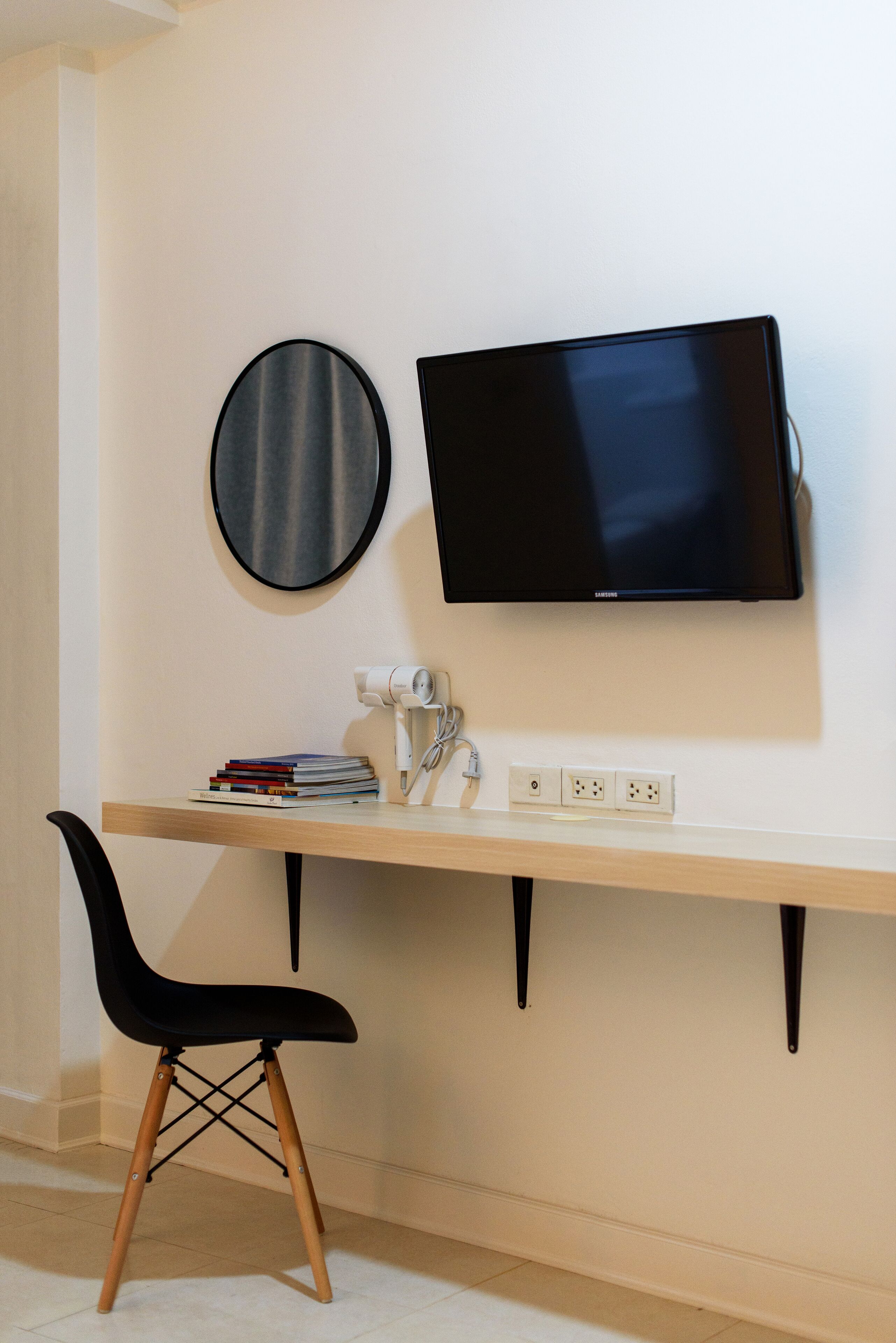 Un espace de travail comprenant un bureau, une chaise, un téléviseur et un miroir rond.