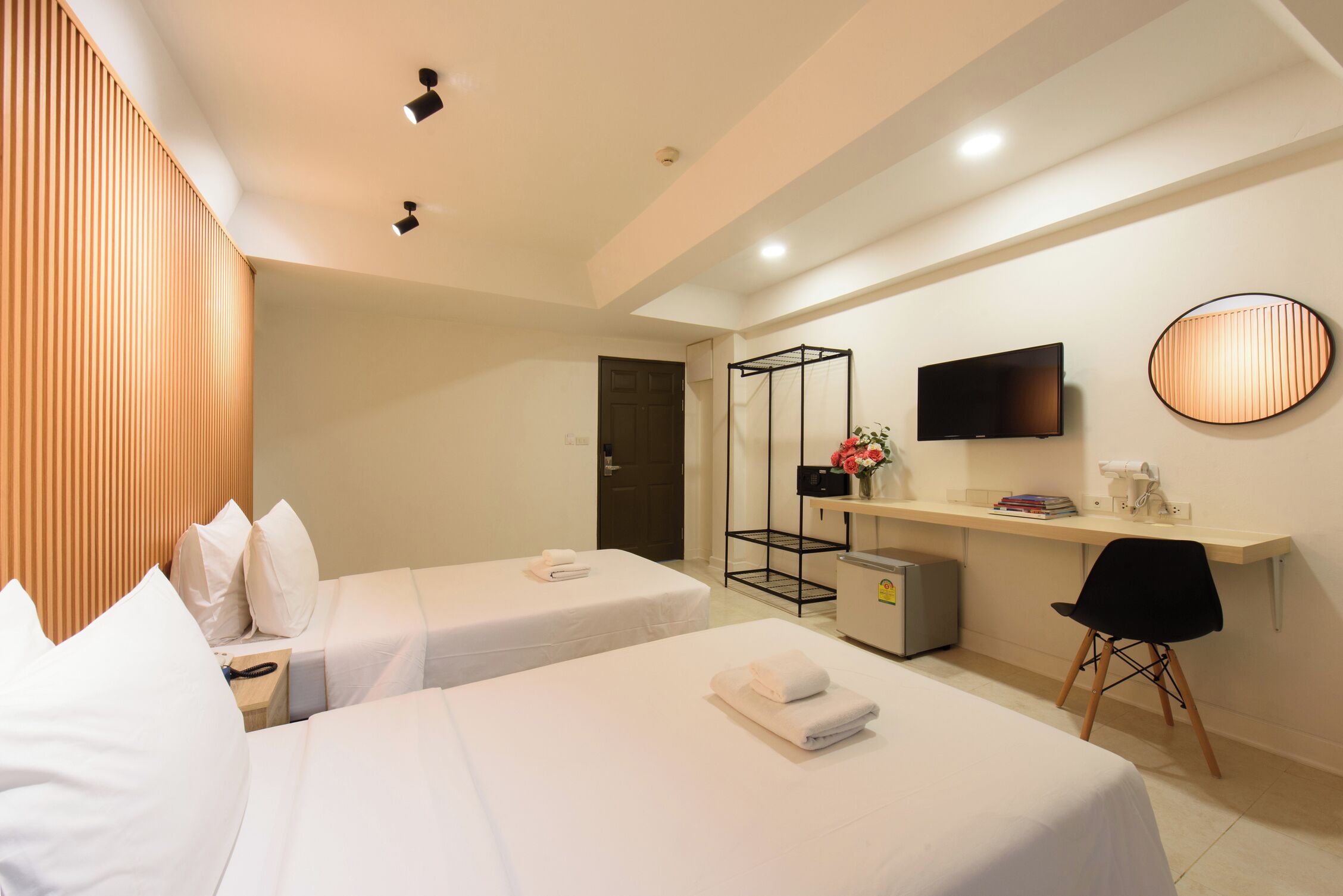 A hotel room with two beds, a desk with a TV, a chair, and a small fridge.