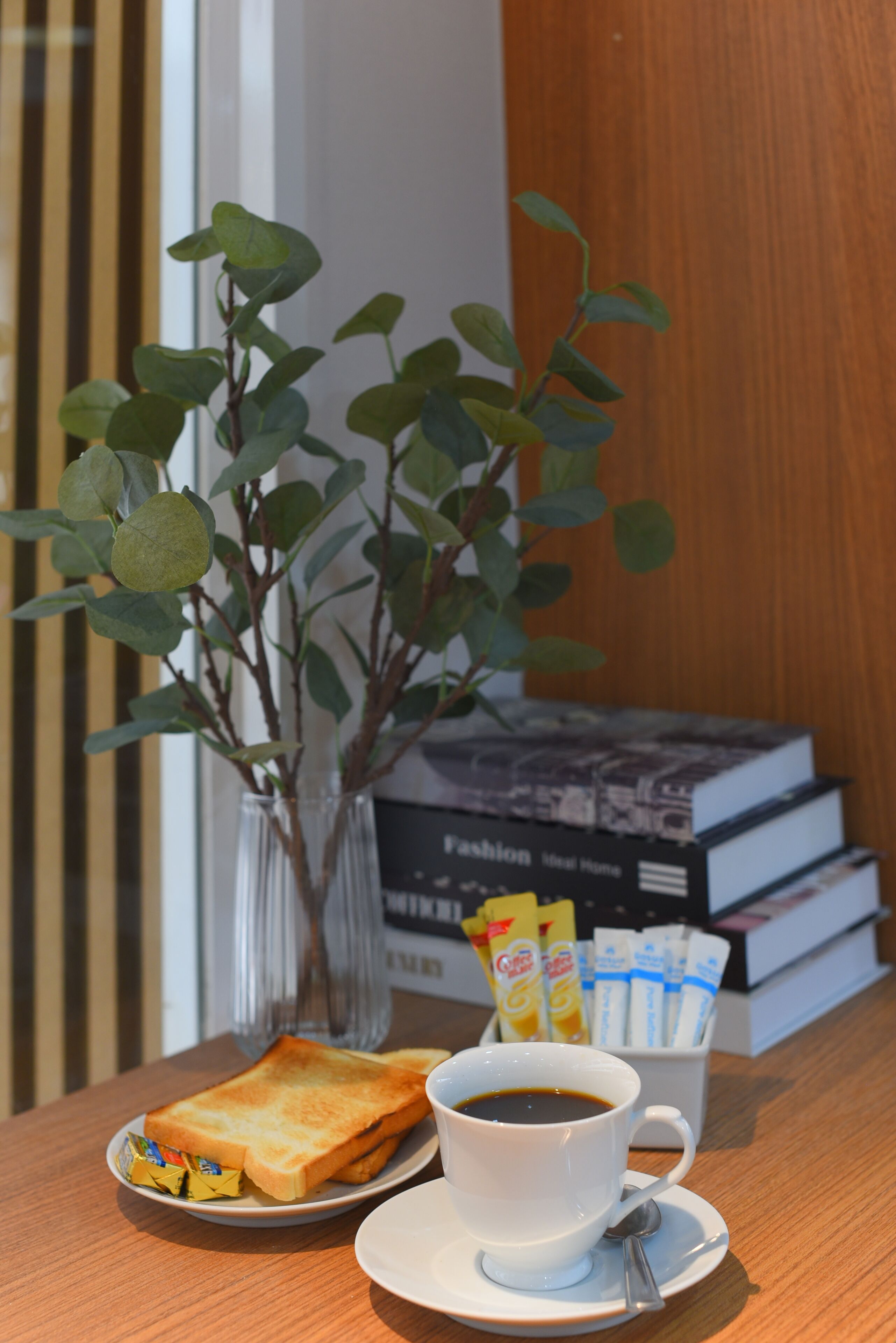 Une table en bois dressée pour le petit-déjeuner, avec des toasts, du café et une plante.