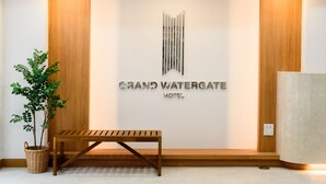 Zona de recepción con un banco de madera, una planta en maceta y un cartel en la pared del Hotel Grand Watergate.