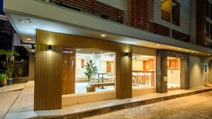 Un hotel moderno con fachada de vidrio, listones de madera y un comedor visible con sillas y mesas.